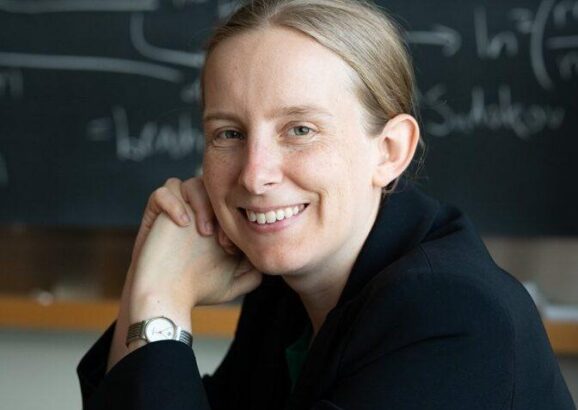 Tracy Slatyer poses in front of blackboard covered in physics equations